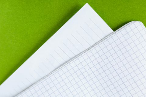 Detailed close-up of white lined and graph paper sheets on a vibrant green background.